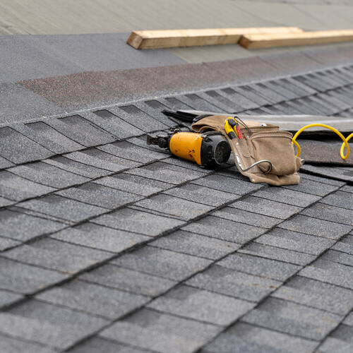 close-up of a tool belt and nail gun on top of a shingle roof