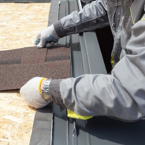 close-up of a worker installing asphalt shingle roofing