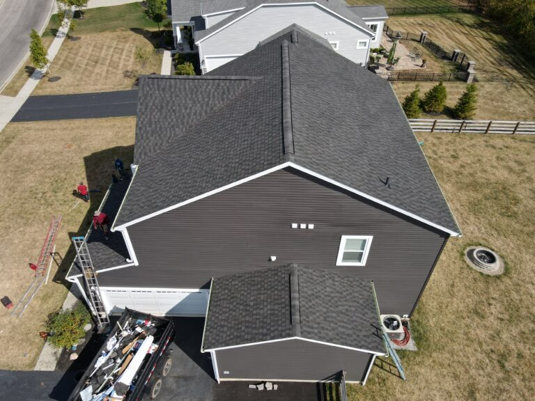 Aerial view of a dark grey shingle roof mid-replacement with a debris trailer below