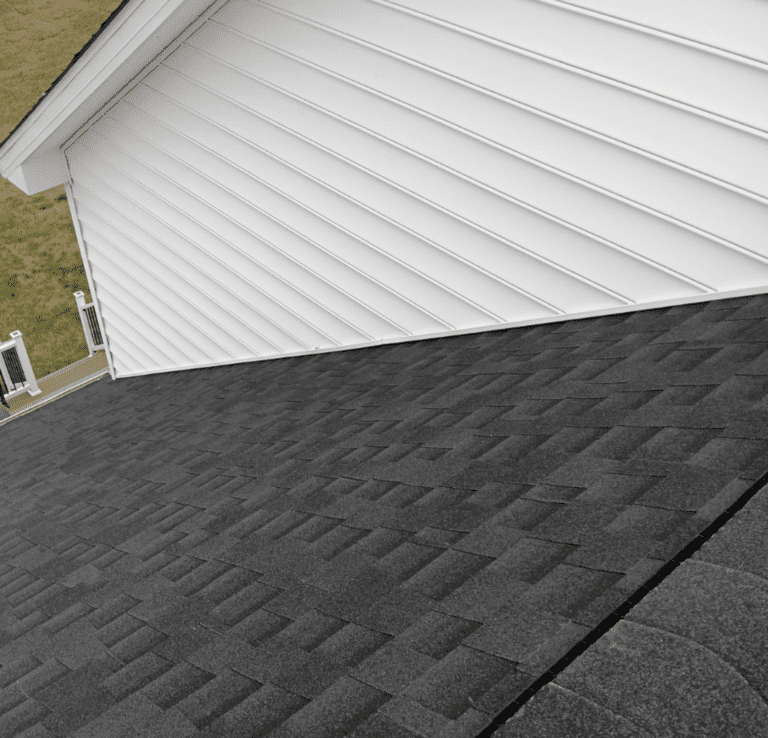 Close-up of newly laid dark architectural shingles meeting white lap siding