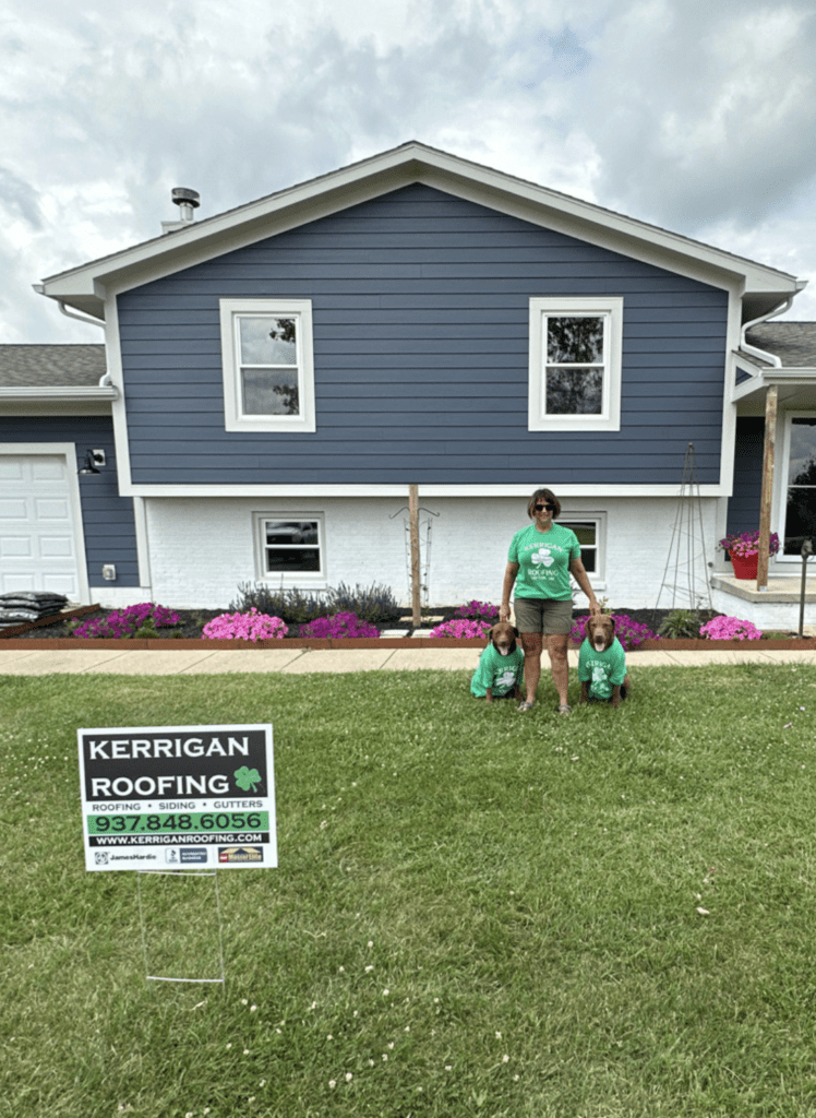 Homeowners outside a blue split-level home with a Kerrigan Roofing yard sign