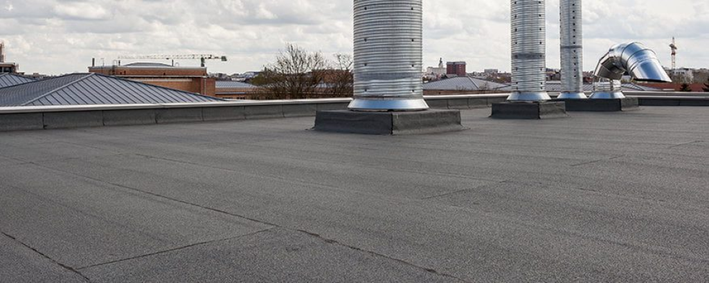 Flat commercial roof with tall metal vent stacks and a city skyline behind