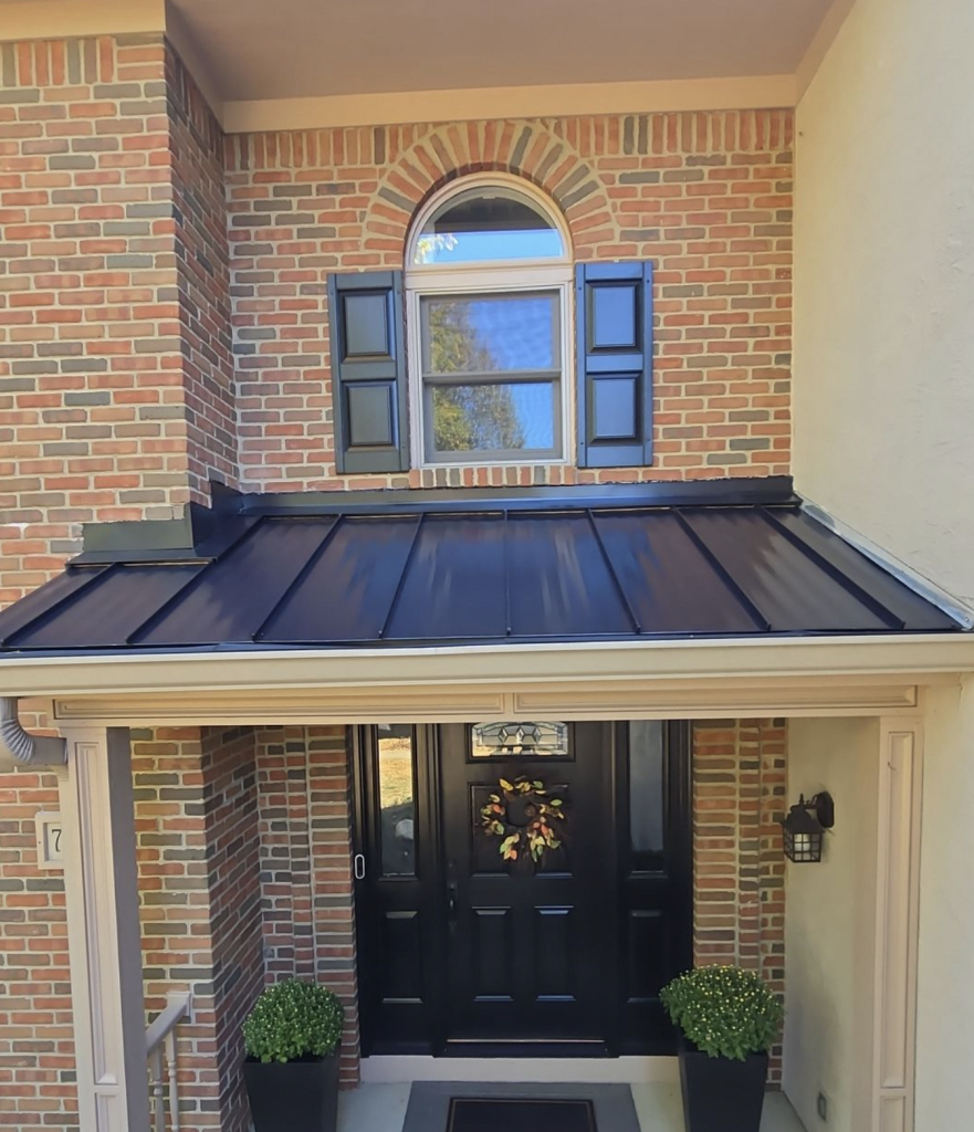 Dark standing seam metal porch roof on a brick home with a shuttered upper window