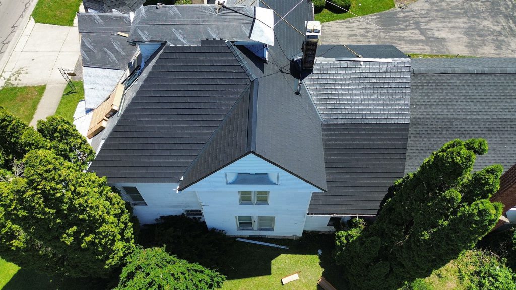 Aerial view of a house part-way through a re-roof, with tarps down and new grey shingles laid