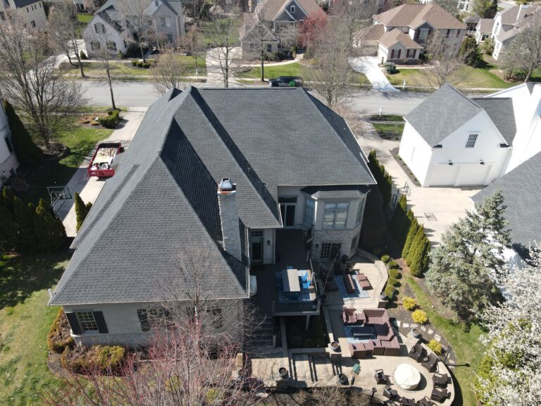 Aerial view of a large stone-clad home with a grey shingle roof and rear patio