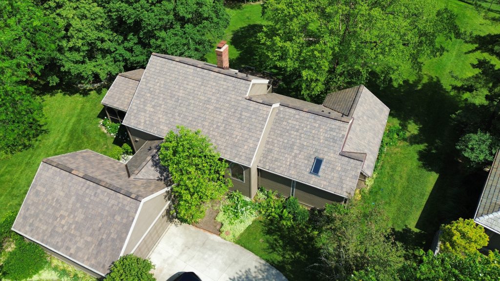 Aerial view of a home with brown and grey blended shake-style shingles among mature trees