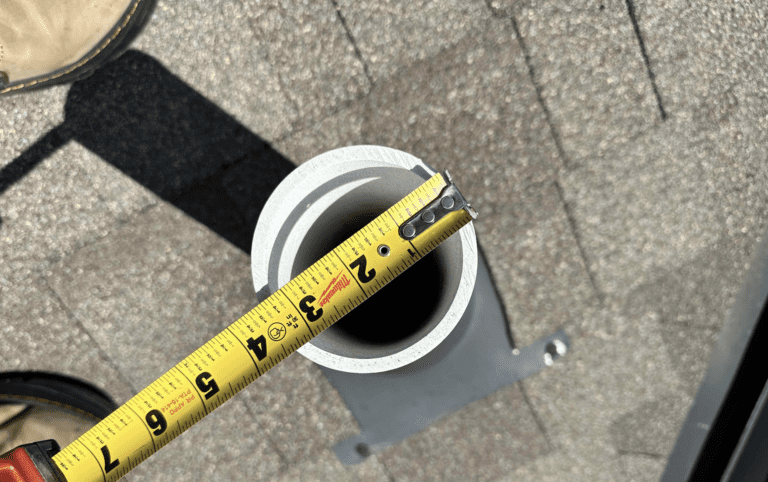 Tape measure held across the opening of a roof vent pipe to check its diameter