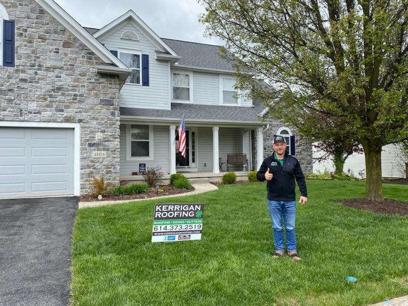 Kerrigan team member giving a thumbs up beside a yard sign outside a finished home