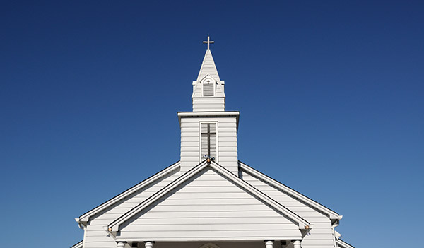 White timber church with a tall steeple against a clear blue sky