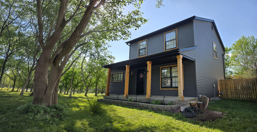 Grey lap-sided two-storey home with a cedar-post porch among mature trees