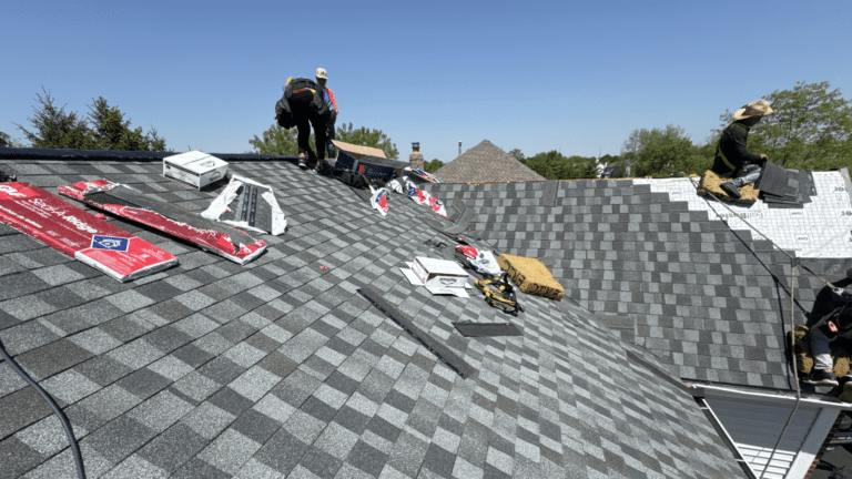 Two roofers installing shingles with GAF bundles staged across the roof