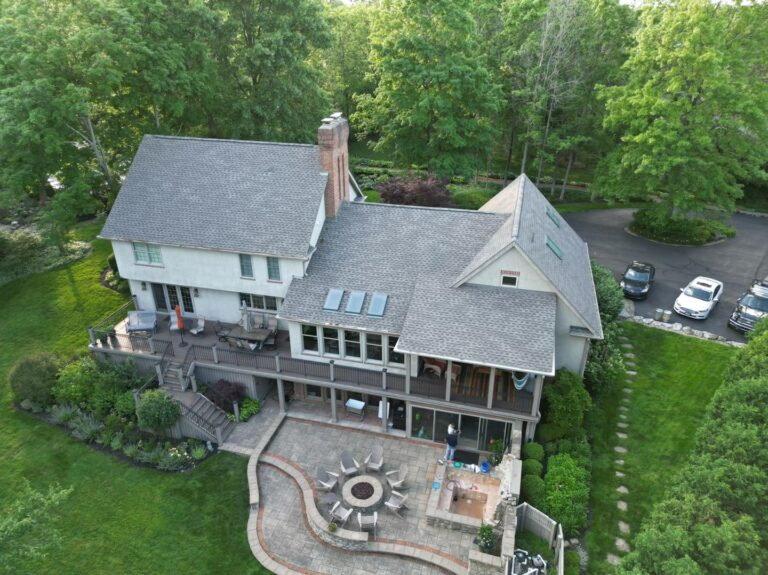 Aerial view of a grey shingle roof with skylights above a paved patio and fire pit
