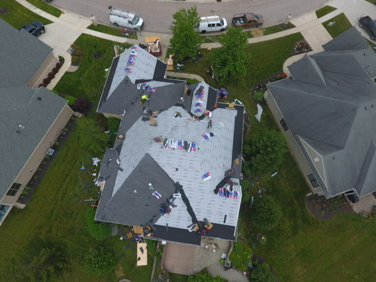 Overhead view of a roof mid-replacement with underlayment exposed and shingle bundles staged