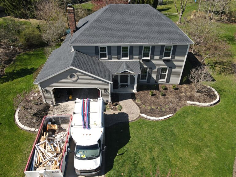 Aerial view of a grey shingle roof replacement with a truck and dumpster on the driveway
